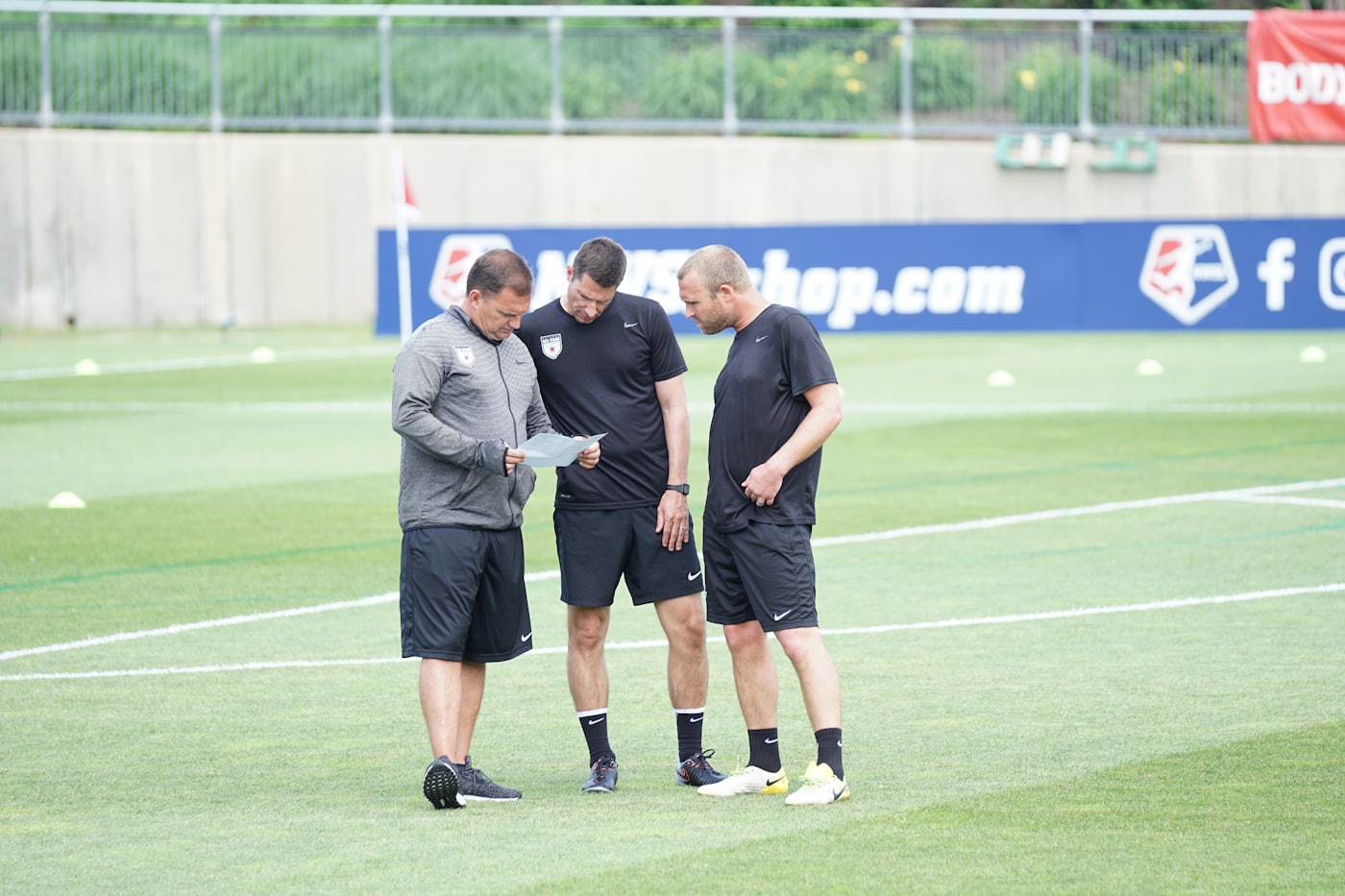 Three coaches standing together on a pitch, looking over notes